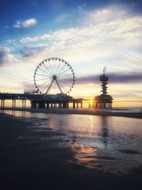 Ferris wheel at sea against cloudy sky