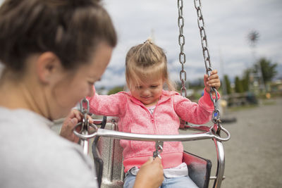 Mother buckling daughter into swing ride.