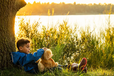 Childhood serenity little boy and cuddly bear by forest lake