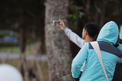 Rear view of woman with man taking selfie in background