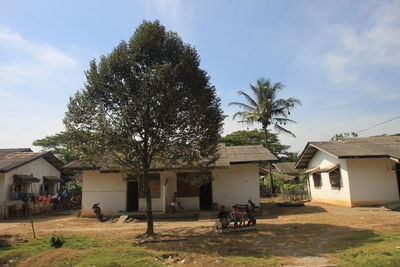 People outside house by tree against sky