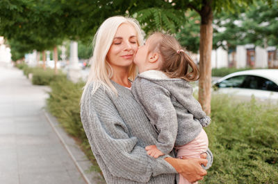 Cute baby child grl 3-4 year old kiss mother walk in city street outdoors. motherhood. 