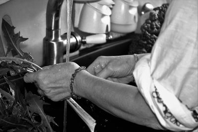 Cropped hands of woman washing leaf vegetable in kitchen sink