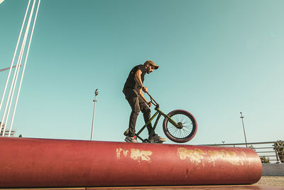 Man riding bicycle on red metallic pipe against sky