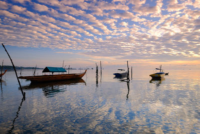 Sailboats moored on sea against sky during sunset