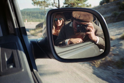 Reflection of man photographing on side-view mirror