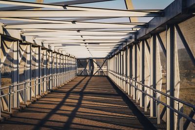 Shadow of railing on bridge against sky