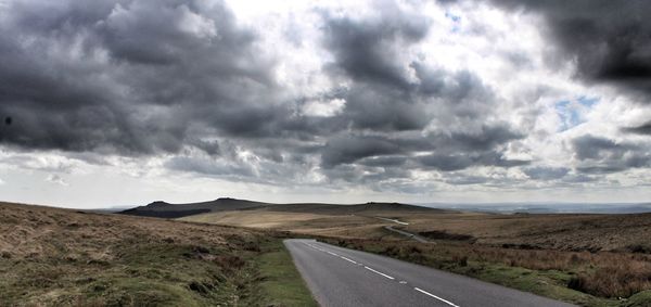 View of road passing through landscape against cloudy sky