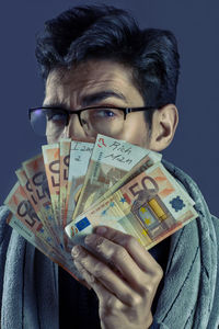 Close-up portrait of man holding eyeglasses against black background