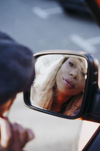 Ethnic female applying makeup near car