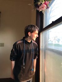 Smiling teenage boy looking through window at home
