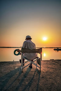 Rear view of man sitting on seat at beach during sunset