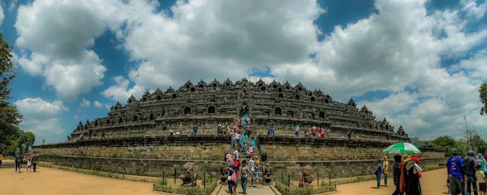 People at historical building against cloudy sky