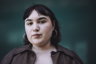 Portrait of young woman wearing nose ring against wall