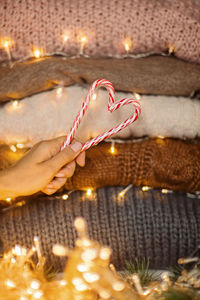 Woman hand holding candy canes, next knitted sweaters, garland light. christmas, xmas