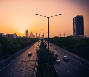 Vehicles on road against sky during sunset