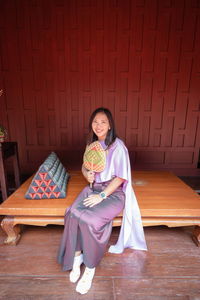 Portrait of smiling woman wearing traditional clothing sitting on wood