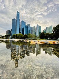 Reflection of modern buildings in lake against sky