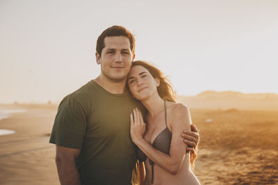 Portrait of young couple standing against sky on beach