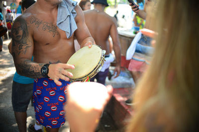 Midsection of shirtless man playing drum outdoors