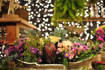 Multi colored flowers in container against lighting decoration at night