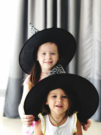 Portrait of sisters wearing hats against curtain