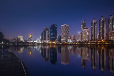 Reflection of illuminated buildings in lake against sky at dusk