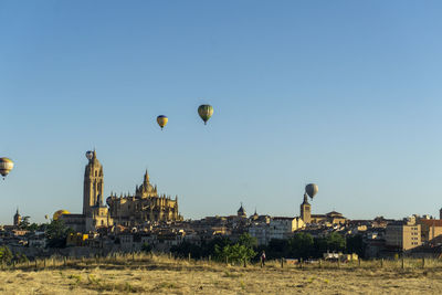 Hot air balloons flying over buildings against blue sky