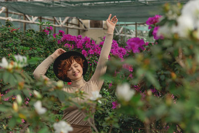 A beautiful plus size girl in a hat enjoying standing among the green plants of the greenhouse. 