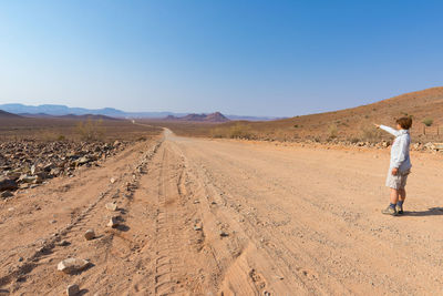 Female tourist standing at desert in namib-naukluft national park against clear sky during sunny day