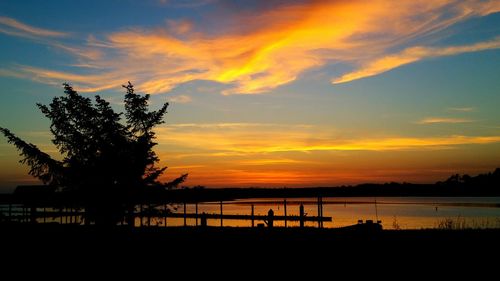 Silhouette trees by sea against orange sky