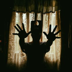 Silhouette man gesturing while standing by curtain