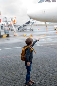 A little boy stands by the plane and points his finger at the pilot.