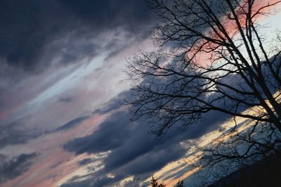 Low angle view of bare trees against cloudy sky