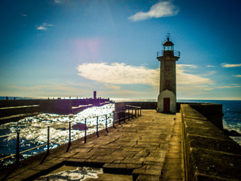 Lighthouse on sea against cloudy sky