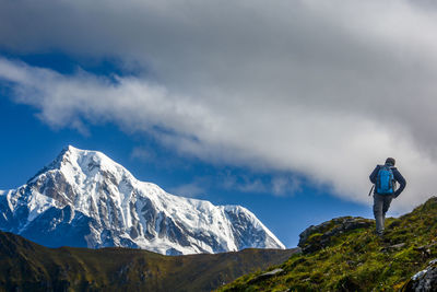 Rear view of man hiking on mountain against cloudy sky