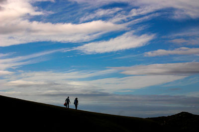 Silhouette people walking on landscape against sky