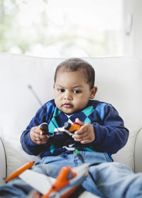 Boy playing with remote controlled airplane on armchair at home