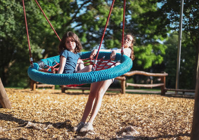 Portrait of two caucasian girls sisters the older one swings the younger one on a round rope swing