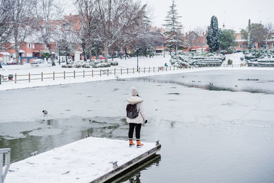 Wide angle view of back view of backpacker woman standing in front of frozen lake in city