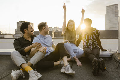 Woman dancing while sitting with male friends on terrace at sunset