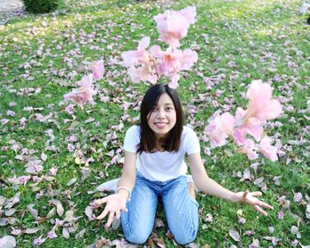 Portrait of smiling young woman sitting on pink flowering plants