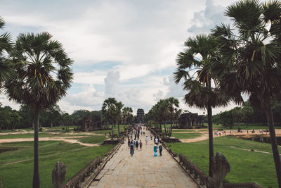 People walking on footpath by palm trees in a temple against sky