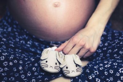 Midsection of pregnant woman with shoes sitting at home