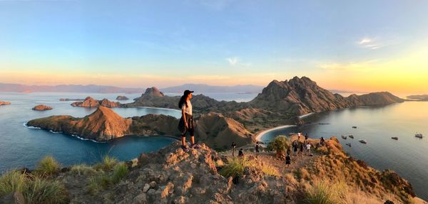 Panoramic image of teenage girl standing on rock looking away during sunset