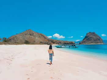 Full length of woman walking on beach against clear blue sky