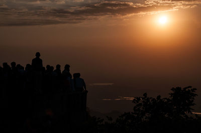 Silhouette people looking at sea against sky during sunset