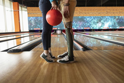 Young woman standing on tiptoes holding bowling ball with boyfriend at alley