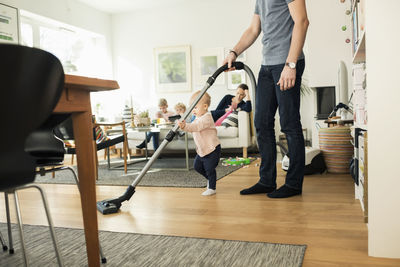 Low section of man and toddler cleaning floor with vacuum cleaner at home