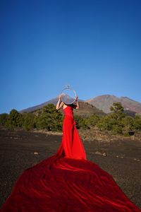 Woman in red dress holding circle while standing against clear sky